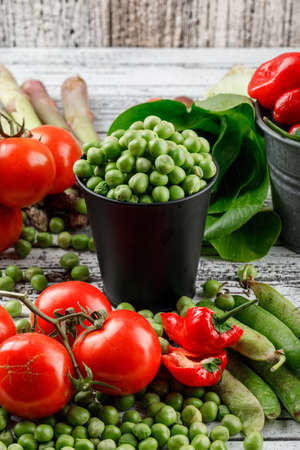Peas in a mini bucket with peppers, tomatoes, asparagus, bok choy, green pods high angle view on a grungy wooden background の写真素材
