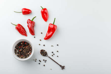 Red peppers with peppercorns in spoon and plate top view on a white backgroundの写真素材