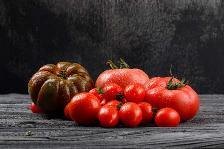 Tomatoes variety on wooden and dark background, side view.