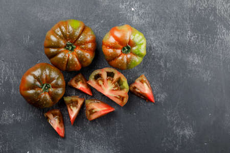 Kumato tomatoes with slices top view on a grungy grey background