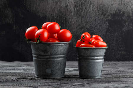 Tomatoes in mini buckets side view on grey wooden and grungy background