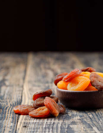 Dried apricots in a clay bowl high angle view on wooden and black background