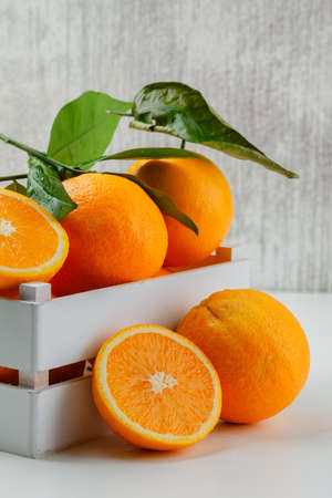 Tasty oranges in a wooden box with branch and slices side view on white and grunge background の写真素材