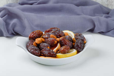 Dates and almonds in a white plate with citrus fruit slices, textile high angle view on grunge and...