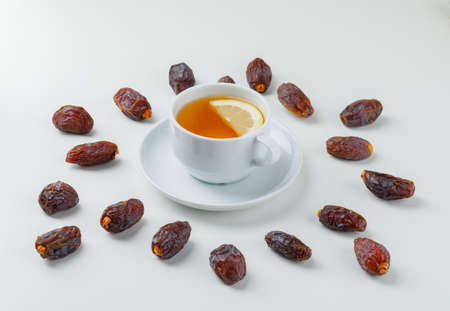 Scattered dates with a cup of lemony tea on white background, high angle view. の写真素材