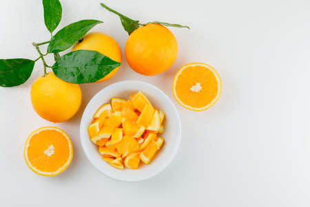 Oranges and slices in a white bowl with branch top view on a white background