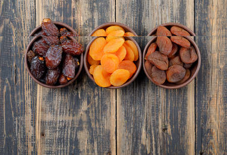 Dried apricots with dates in clay bowls on wooden background, top view.の写真素材