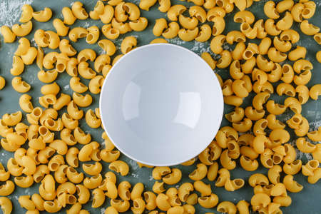 Empty bowl on scattered pasta and greenish background. top view.