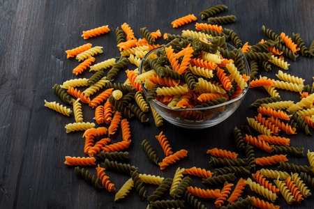 Colored fusilli pasta in a glass bowl on a wooden background. high angle view.