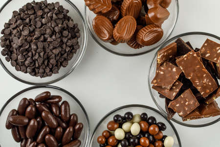 Chocolate and candies in glass bowls on white background, flat lay.