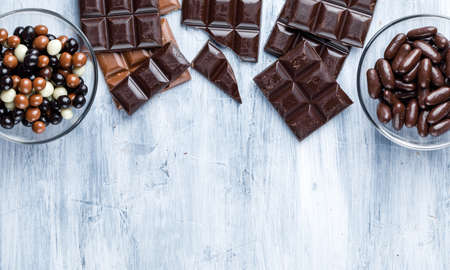 Chocolate bars with candies in glass bowls on grungy background, top view.