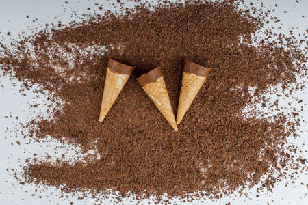 Sweety chocolate in cones on white and grated chocolate background, flat lay.