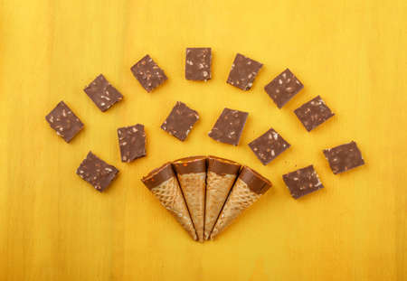 Chocolate bars with candies in waffle cones on yellow wooden background, flat lay.の写真素材