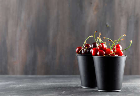 Cherries in mini buckets side view on grunge and grey backgroundの写真素材