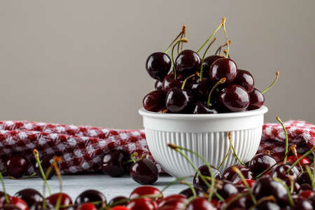 Black cherries in a bowl with picnic cloth side view on grungy and grey backgroundの写真素材