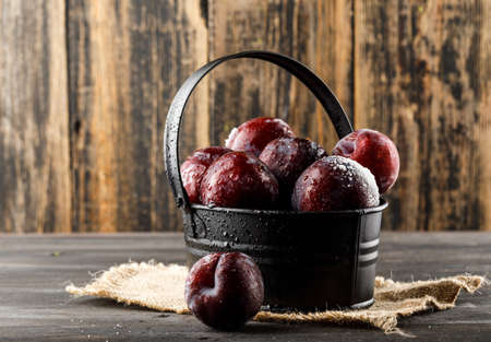 Red plums with piece of sack in a basket on wooden and grungy background, side view. の写真素材
