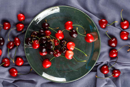 Fresh cherries in a plate on textile background, top view.の写真素材