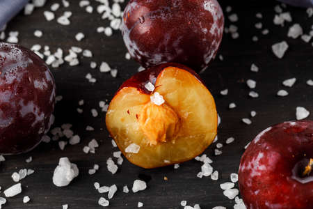 Ripe plums with rock salt, textile close-up on a grey backgroundの写真素材