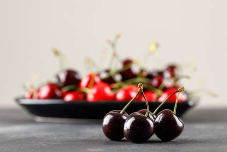Cherries in a plate on white and grey background, side view.
