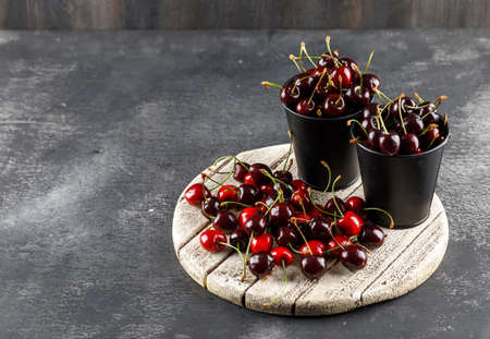 Cherries with wooden board in buckets on grungy and wooden background, high angle view.