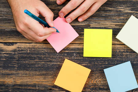 Business concept with sticky notes on wooden backgroud flat lay. man writing with pen.