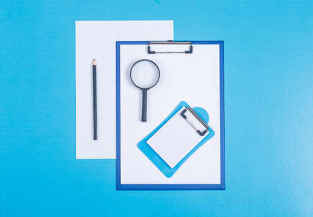 Finance and accounting concept with paper holder, pencil, notepad, paper, magnifier on cyan blue background top view. horizontal imageの写真素材
