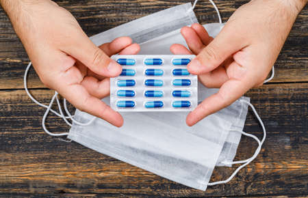 Medical concept with face masks on wooden backgroud flat lay. man holding pack of capsules.の写真素材