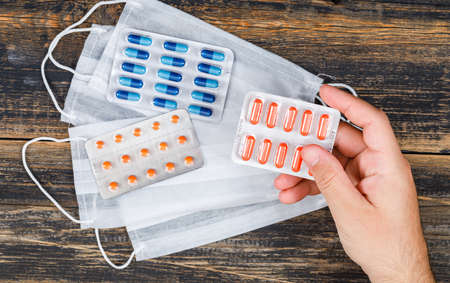 Medical concept with medicines, face masks on wooden backgroud flat lay. man holding pack of capsules.の写真素材