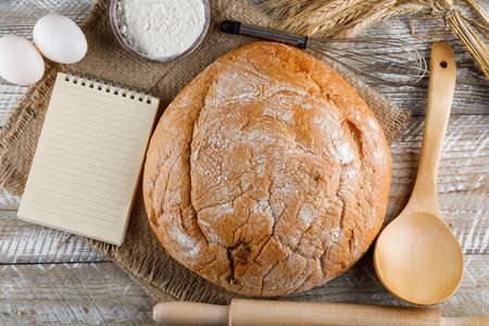 Bakery product with eggs, rolling pin, notepad, spoon, flour top view on a wooden background 