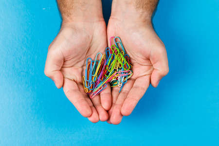 Business and financial concept with paper clips on the palm on blue background flat lay.
