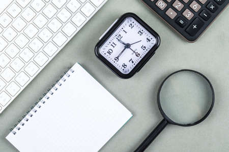 Time and money concept with keyboard, calculator, magnifier, notebook, watch on navy green...