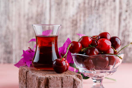 Cherries in a vase with flowers, glass of tea on brick side view on pink and grungy background 