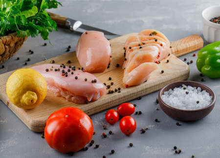 High angle view chicken breasts on cutting board with lemon, tomatoes, salt on gray background. horizontalの写真素材