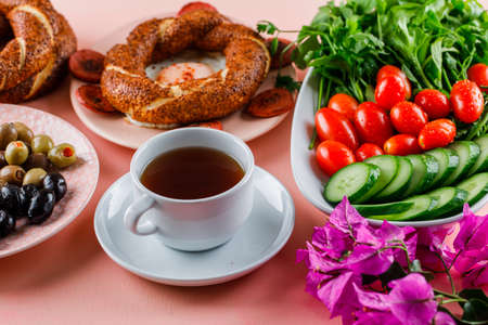 Eggs with sausage in a plate with a cup of tea, turkish bagel, olive, salad, flowers on pink background, high angle view. の写真素材