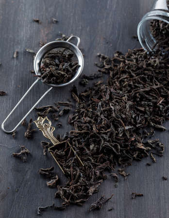 Black dry tea in strainer, jar, scoop on a wooden background. high angle view. の写真素材