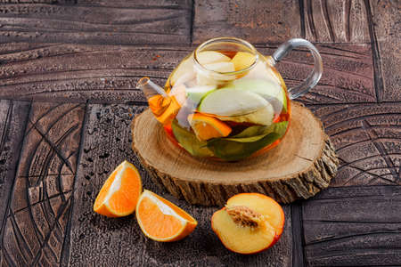 Fruit infused water with fruits, wooden piece in a teapot on stone tile background, high angle view.の写真素材