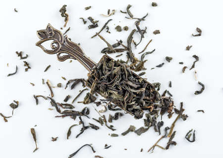 Green tea leaves in a copper scoop flat lay on a white background