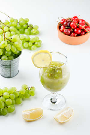 Cherries and grapes with lemon slices, grape cocktail in bucket and bowl on white background, high...