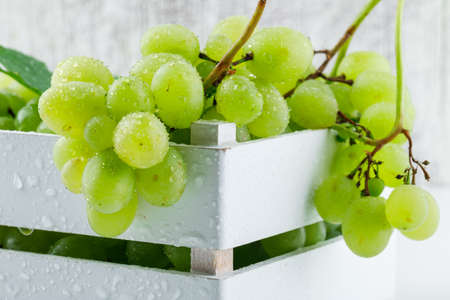 Fresh grapes with leaves in a wooden box on white and grungy background, side view.