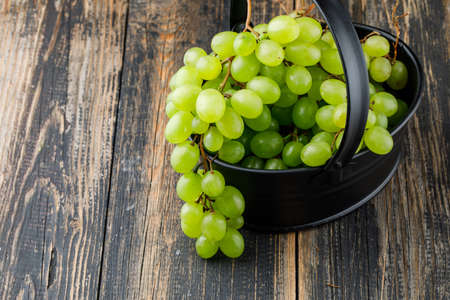 Grapes in a black basket on wooden background, high angle view.の写真素材