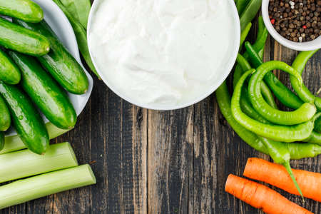 Cucumbers and yogurt in plates with carrots, peppercorns, peppers, celery, green beans flat lay on a...