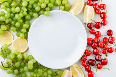 Green grapes with lemon slices, cherries, plate on white background, top view.の写真素材