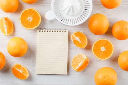 Oranges and slices with squeezer, copybook on white wooden background, top view.の写真素材