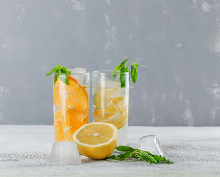 Icy detox water with orange, lemon, mint in glass on plaster and grunge background, side view. の写真素材