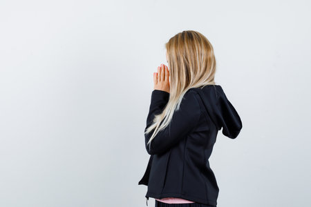 blonde girl clasping hands in prayer position in pink t-shirt and black jacket and looking focused , front view.の写真素材
