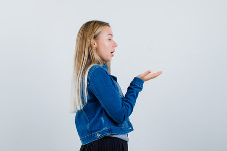 young female pretending to hold something in t-shirt, denim jacket, skirt and looking amazed , front view.の写真素材