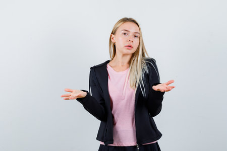 blonde girl stretching hands in questioning manner in pink t-shirt and black jacket and looking baffled , front view.の写真素材