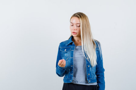 young lady in t-shirt, denim jacket, skirt looking at hand and looking thoughtful , front view.の写真素材