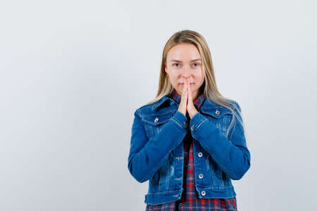 blonde lady holding hands in praying gesture in shirt, jacket and looking hopeful , front view.の写真素材