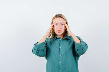young lady holding hands on temples in green shirt and looking depressed. front view.